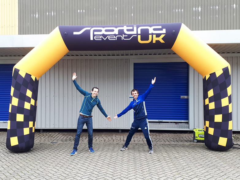 Two men stood under an inflatable race arch