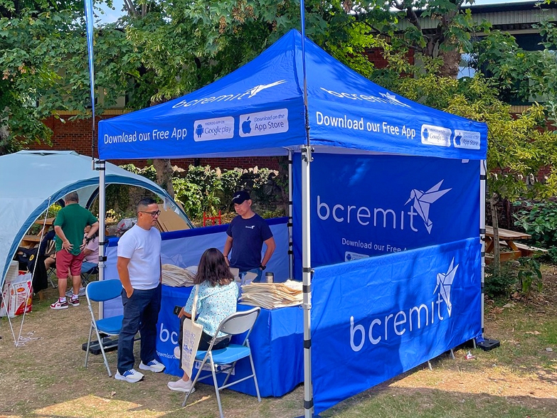BCRemit 3m x 3m Trader Plus Package gazebo with teardrop flags and branded half walls at outdoor event